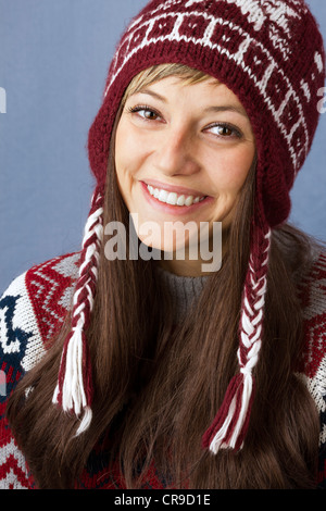 Attractive young woman with a beautiful bright smile wearing pullover and wool cap. Portrait against a light blue background Stock Photo