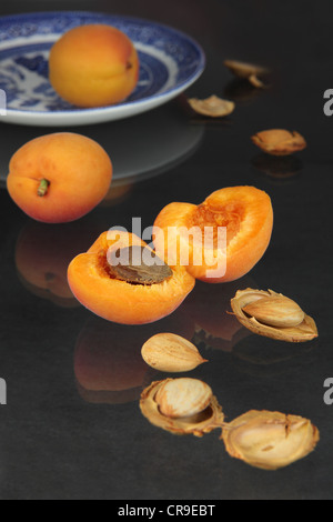 Apricots and kernels on a black reflective table. Some kernels are hulled, one fruit is on a plate Stock Photo