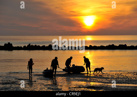 Fishermen landing on beech in Combe Martin, North Devon, silhouetted against bright orange sky of sunset. Stock Photo