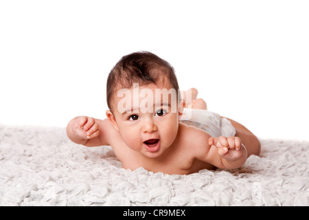 Cute happy baby laying on belly on soft surface wearing diaper, looking at camera, isolated. Stock Photo
