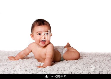Cute happy smiling baby laying on belly on soft surface wearing diaper, isolated. Stock Photo
