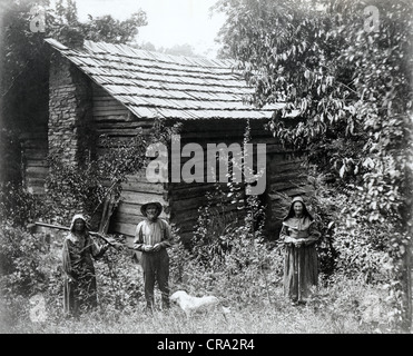 Elderly Couple & Adult Daughter in front of Ancient Log Cabin Stock Photo