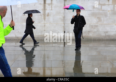 people walking passed a plain wall in the rain Stock Photo