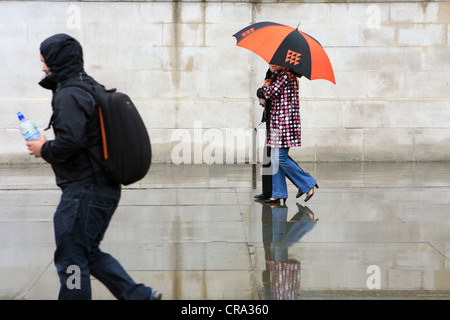 people walking passed a plain wall in the rain Stock Photo