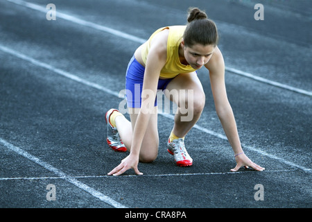 Athletic teenage girl in start position on track. Concept of