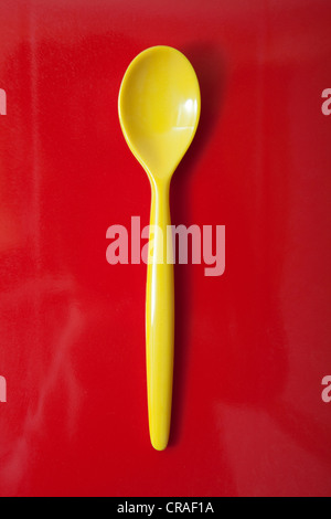 Yellow plastic spoon, egg spoon, on red Stock Photo
