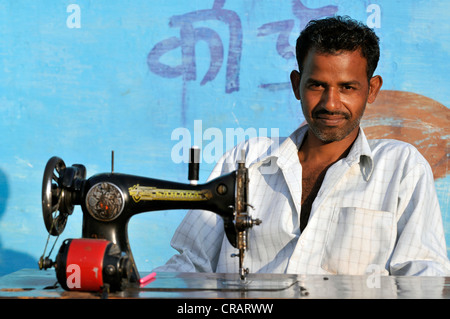 Man sitting at a sewing machine in front of a blue wall, portrait, Orchha, Madhya Pradesh, northern India, India, Asia Stock Photo