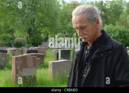 Sorrowful man standing in cemetery with head bowed Stock Photo