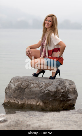 Young smiling blond woman wearing hotpants posing on a stone in water Stock Photo