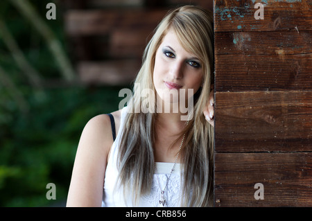 Young woman with long blonde hair standing next to a wooden wall, portrait Stock Photo