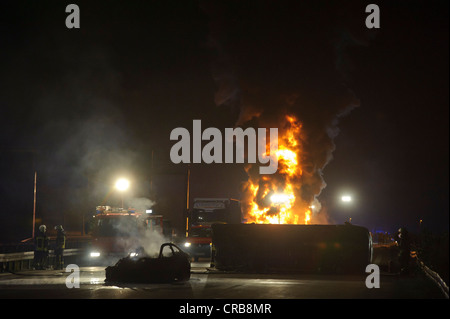 A fully burnt-out BMW sports car beside a transport van lying on its side in front of a burning truck and an oil tank truck Stock Photo