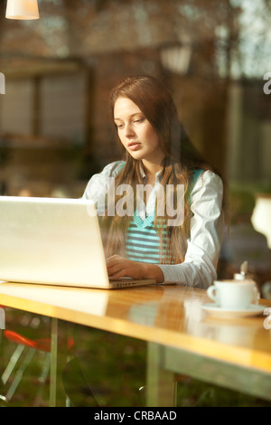 Student with a laptop sitting in a cafe, seen through a window Stock Photo