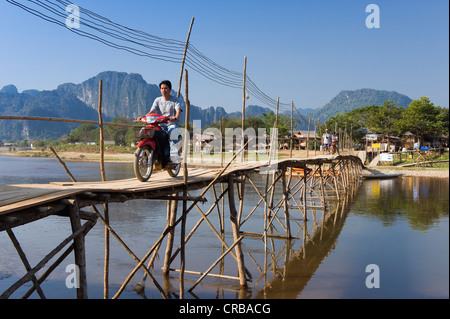 Moped rider crossing the bamboo bridge over the Nam Song River, karst mountains, Vang Vieng, Vientiane, Laos, Indochina, Asia Stock Photo