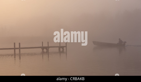 Dock and boat in the fog on Lake Staffelsee with the island of Woerth near Seehausen, Murnau, Upper Bavaria, Bavaria Stock Photo