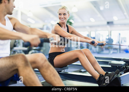 Couple using rowing machines in gym Stock Photo