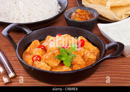 Indian curry butter chicken with rice, poppadums, mango chutney and cucumber raita. Stock Photo