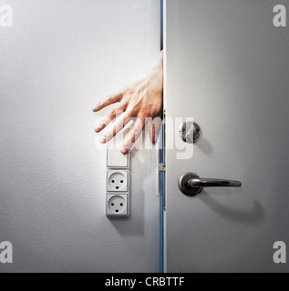 Hand turning off light from behind door Stock Photo