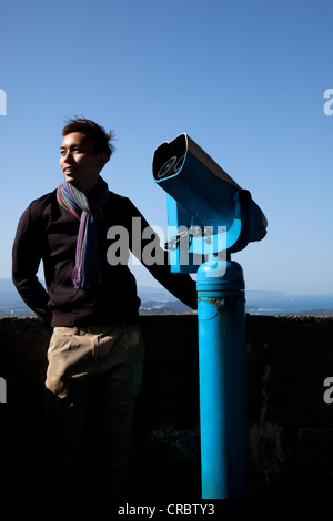 Man with scarf around neck, standing next to a telescope Stock Photo