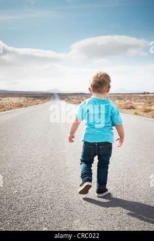 Boy walking on paved rural road Stock Photo