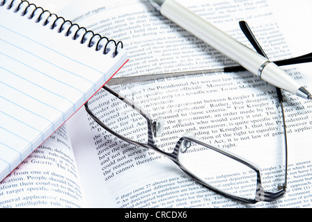 Notebook pen and reading glasses on an open book. Stock Photo