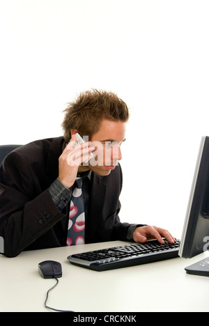 young businessman in his office, working on his computer and using his mobile Stock Photo