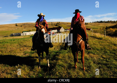 Two cowgirls with handkerchiefs over their faces sitting on horses, Saskatchewan, Canada, North America