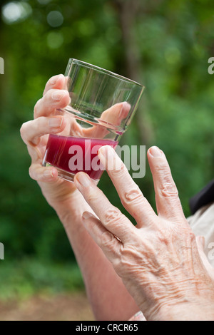 Hand holding a glass with red juice, old lady's hands Stock Photo