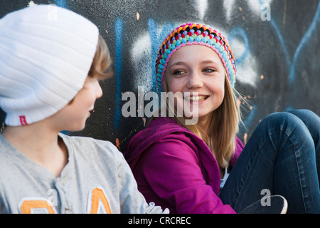 Teeange girl and boy sitting at graffiti wall Stock Photo