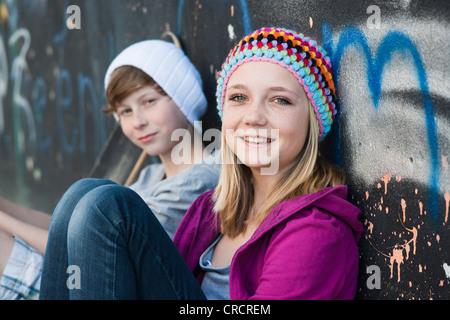 Teeange girl and boy sitting at graffiti wall Stock Photo