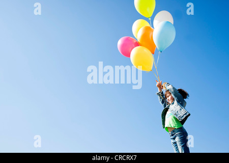 Girl standing with balloons under blue sky Stock Photo