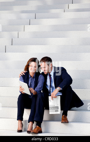 Businessman and businesswoman tablet PC and newspaper on stairs Stock Photo