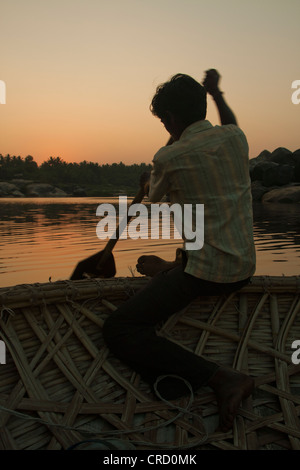 Boy rowing a coracle reed boat - Hampi, India at Sunset Stock Photo - Alamy