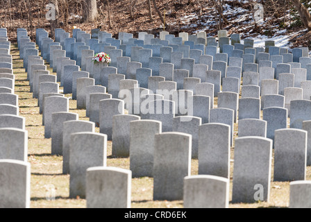 One flower topped Grave Stands out.  A bouquet of flowers causes one of hundreds of identical grave markers to stand out Stock Photo