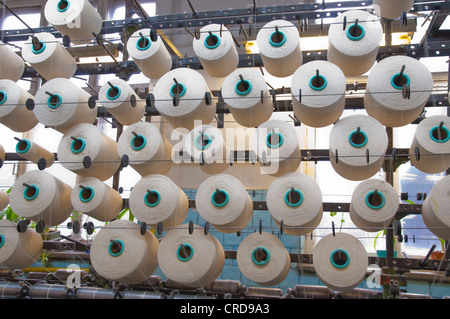 Cotton yarn on large spools and textile factory equipment in the workshop Stock Photo