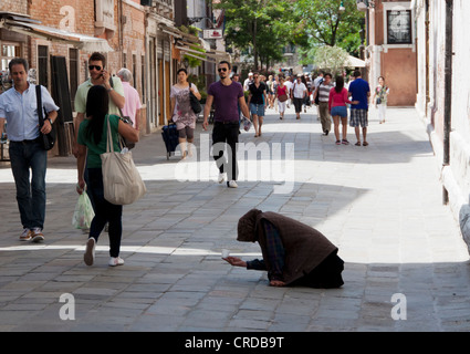 A woman begging on the Venice street amongst passing tourists Stock Photo