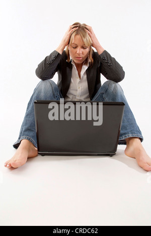 desperate woman sitting in front of her laptop, with her hands on head Stock Photo