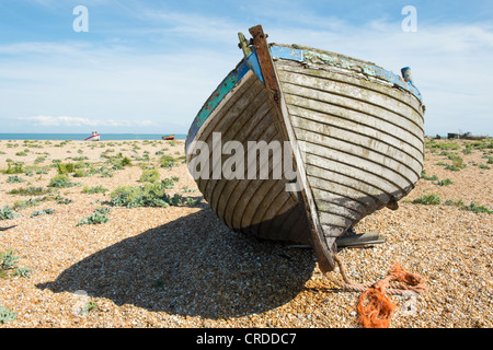An old wrecked wooden fishing boat on a shingle beach under the light ...