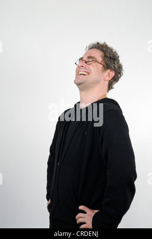 Young man with glasses laughing heartily, hands on hips Stock Photo