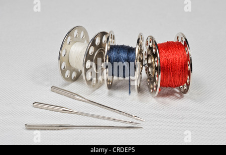 Sewing machine needles fanned out with yarn spools lying on white linen fabric Stock Photo