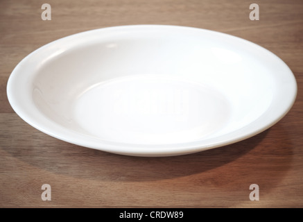 Empty white plate at angle on the wooden table Stock Photo