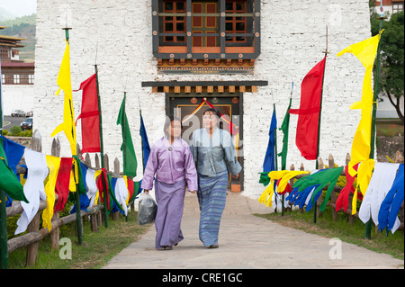 Two women dressed in traditional costume, coloured flags lining a path, fortress-monastery, Dzong, Punakha, the Himalayas Stock Photo