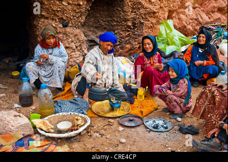 Nomadic cave-dwellers sitting in front of their cave-dwelling, a man wearing a blue turban is pouring tea into a pot on a copper Stock Photo