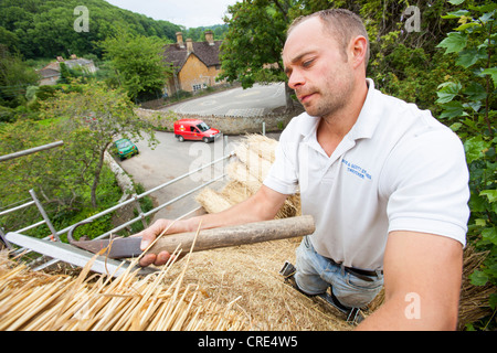 A skilled thatcher thatching a barn roof in Dorset, UK Stock Photo