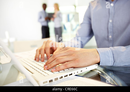 Image of human hands typing in the foreground, business colleagues can be recognized in the blurred background Stock Photo