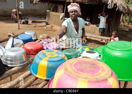 A woman sets bowls, pots and dishes on an elevated dish rack, used to dry dishes instead laying them directly on the ground Stock Photo