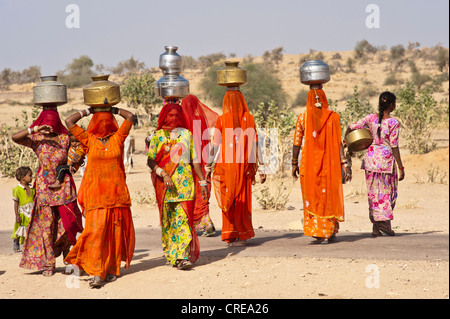 Young veiled Indian women wearing saris, carrying water jugs from the well on their heads, Thar Desert, Rajasthan, India, Asia Stock Photo