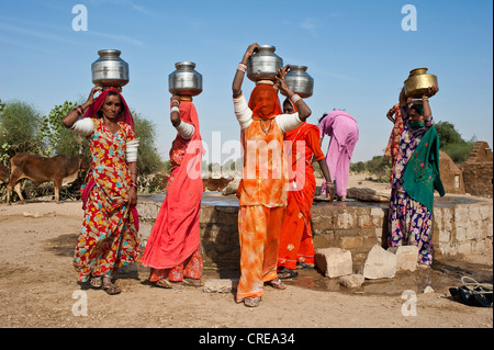 Indian women wearing saris carrying water jugs on their heads, they just filled the jugs at the well, Thar Desert, Rajasthan Stock Photo