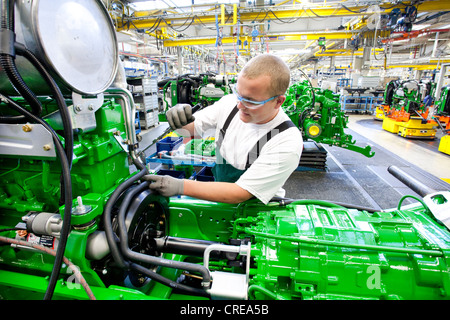 Worker is connecting hoses between the engine and the gearbox in the engine assembly area of the tractor production section at Stock Photo