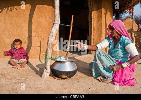 An elderly woman wearing a sari sitting on the floor, she is preparing lassi, yogurt with a traditional whisk, lassi is made Stock Photo