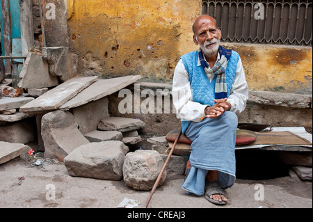 Elderly Indian man, Rajasthani, sitting on a stone bench with cushions in front of a house, resting, Bundi, Rajasthan, India Stock Photo